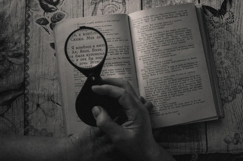 a person holding a magnifying glass over an open book, a black and white photo, pexels contest winner, hyperrealism, instagram story, words, vintage horror, vantablack chiaroscuro