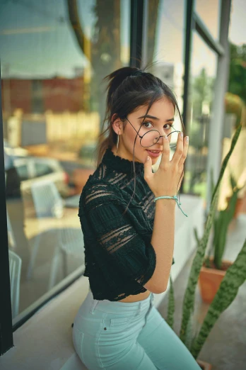 a woman sitting on a window sill smoking a cigarette, a picture, by Robbie Trevino, trending on pexels, isabela moner, with square glasses, black and green, postprocessed)