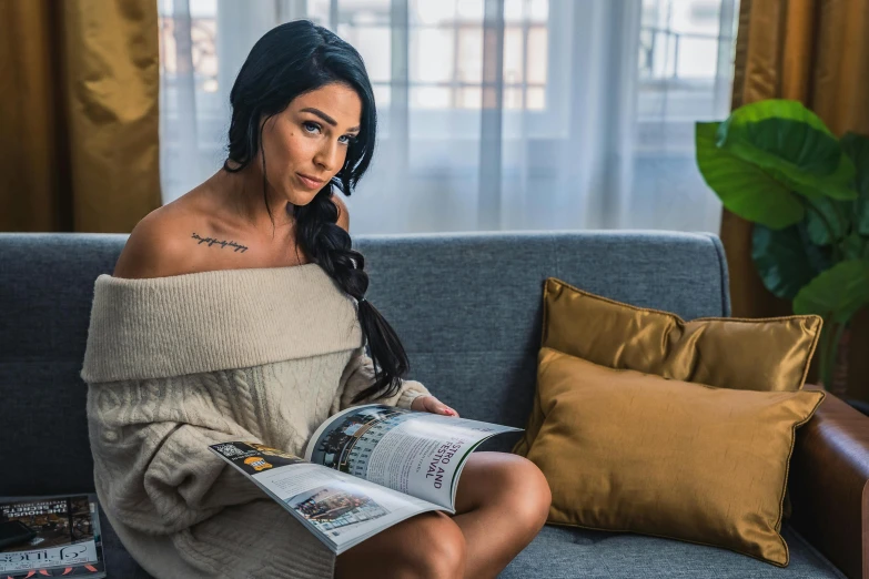 a woman sitting on a couch reading a magazine, a portrait, by Adam Marczyński, trending on pexels, arabesque, portrait of demi rose, arab ameera al-taweel, tattooed, hotel room