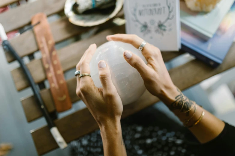 a woman holding a white ball on top of a wooden table, a marble sculpture, trending on pexels, spell casting wizard, magical notes, full of things, a wizard's apothecary