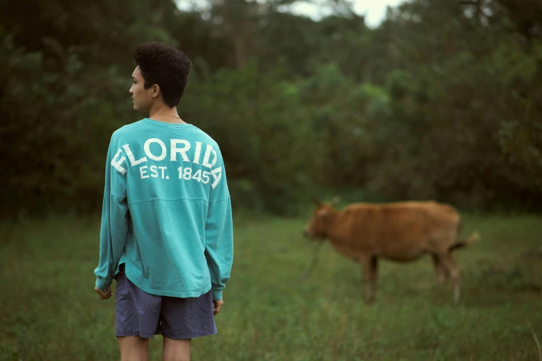 a man standing in a field next to a cow, inspired by Elsa Bleda, visual art, florida, long sleeves, seafoam green, florida man