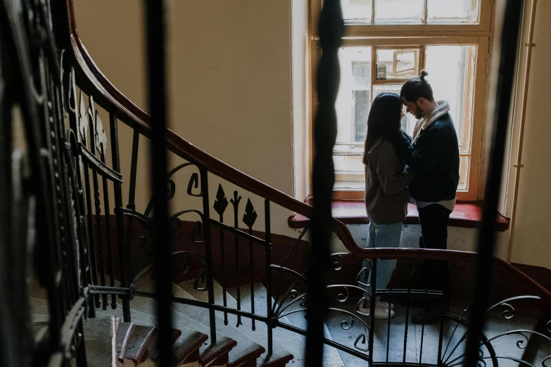 a man and a woman standing on a set of stairs, a picture, by Emma Andijewska, pexels contest winner, art nouveau, making out, inside the building, promo image, cozy