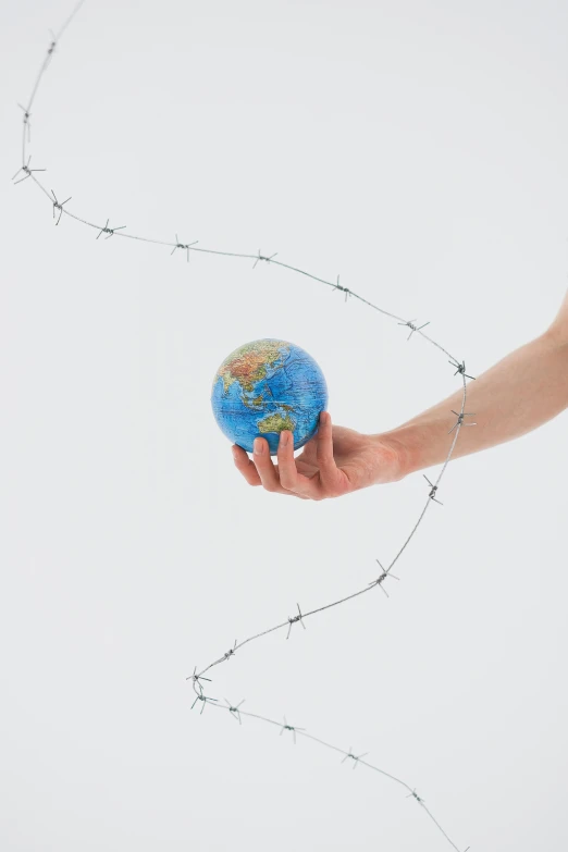 a person holding a small globe in their hand, an album cover, inspired by Scarlett Hooft Graafland, conceptual art, barbed wire, taken in the early 2020s, plain background, ai biodiversity