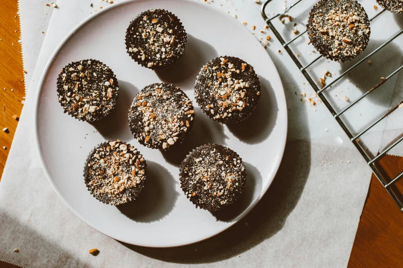 a white plate topped with chocolate cupcakes next to a cooling rack, unsplash, mingei, gold speckles, thumbnail, snacks, crackles