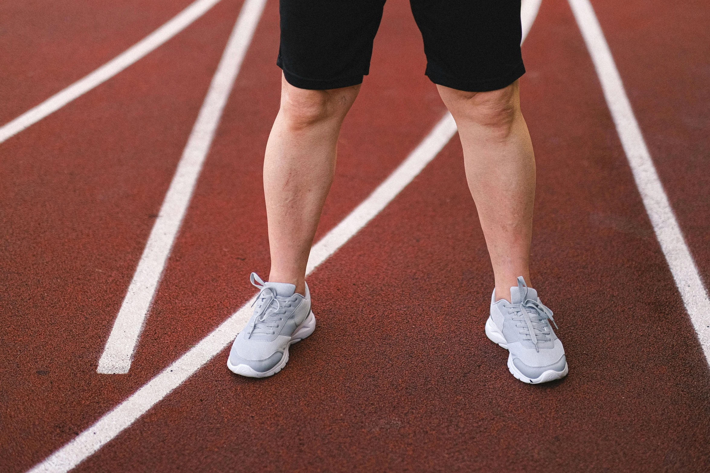 a man standing on a track holding a tennis racquet, looks like varicose veins, running shoes, rectangle, high arches