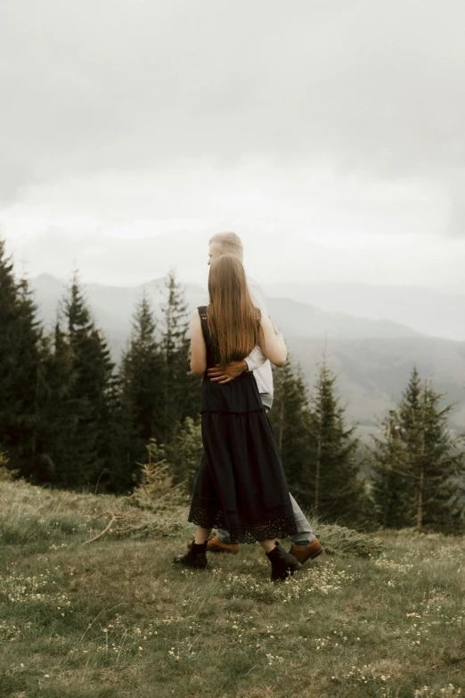a woman standing on top of a lush green hillside, pexels contest winner, romanticism, hugging each other, grey forest in the background, back, concert