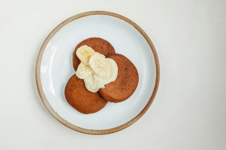 a white plate topped with cookies and banana slices, inspired by Richmond Barthé, unsplash, bao pnan, bronze poli, brown, pancakes