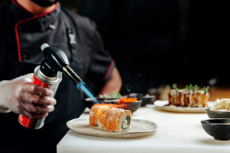 a chef sprays down on a plate of sushi, an airbrush painting, by Niko Henrichon, pexels, holding a torch, foam, creating a soft