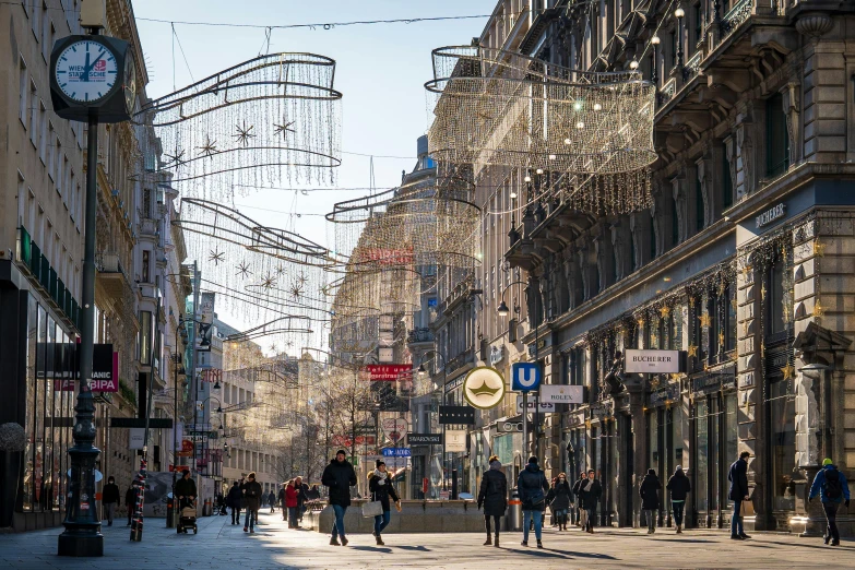 a group of people walking down a street next to tall buildings, pexels contest winner, viennese actionism, chandeliers, holiday season, wires hanging above street, prefecture streets