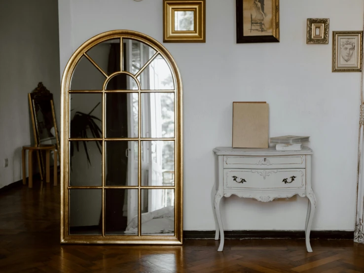 a mirror sitting on top of a table next to a dresser, inspired by Constantin Hansen, pexels contest winner, art nouveau, arched doorway, steel window mullions, gold plated, tightly framed