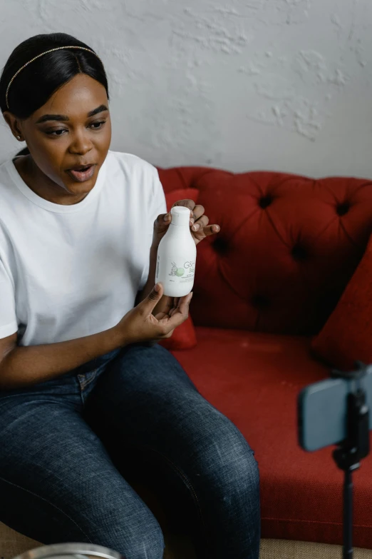 a woman sitting on a couch holding a bottle, a picture, happening, photoshoot for skincare brand, video footage, photo of a black woman, medium shot taken from behind