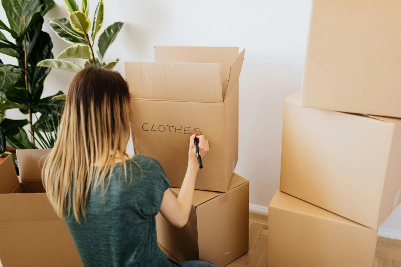 a woman is writing clothes on a cardboard box, by Eden Box, pexels contest winner, exiting from a wardrobe, thumbnail, sharpie, family friendly