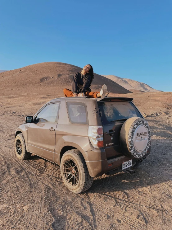 a man sitting on top of a car in the desert, her face is covered with mud, profile image, square, andes