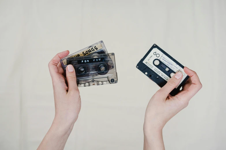 a person holding a cassette in their hands, by Emma Andijewska, trending on pexels, then another, old tape, high samples, black on white background