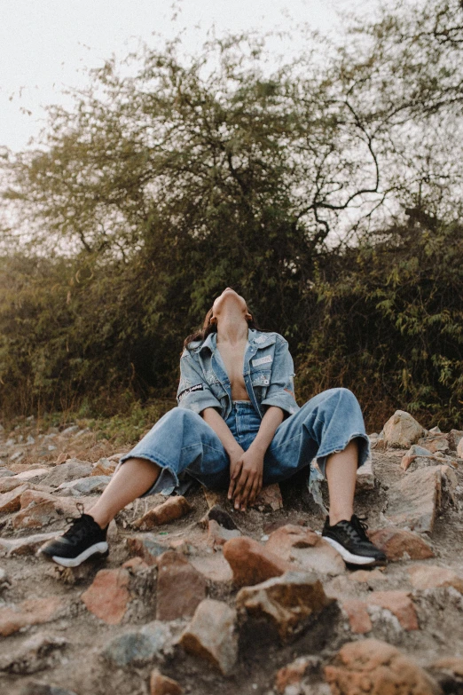 a woman sitting on top of a pile of rocks, trending on pexels, realism, wearing denim, androgynous male, stressing out, 2019 trending photo
