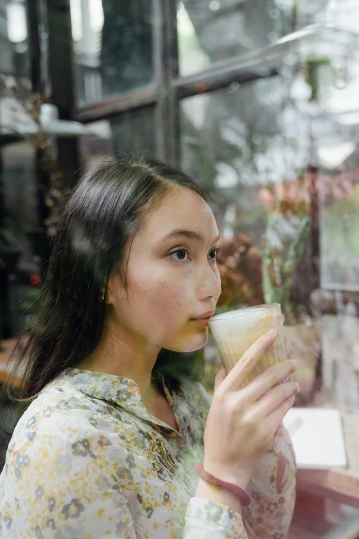 a woman sitting in front of a window eating a sandwich, inspired by Tan Ting-pho, pexels contest winner, sumatraism, iced latte, profile image, 1 6 years old, drinking cocktail