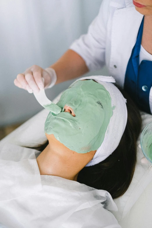 a woman getting a facial mask at a spa, by Nicolette Macnamara, pastel green, cast, no face mask, green