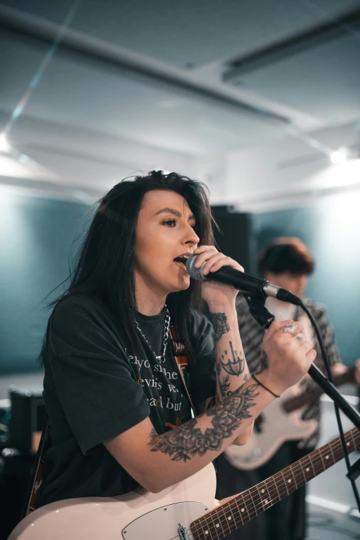 a woman singing into a microphone while holding a guitar, pexels contest winner, antipodeans, charli bowater and artgeem, with tattoos, profile image, in a room