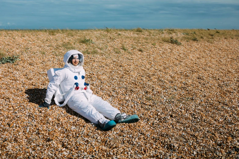 a person in an astronaut suit laying on the ground, unsplash, seaside, mrs bean, lunar themed attire, prince