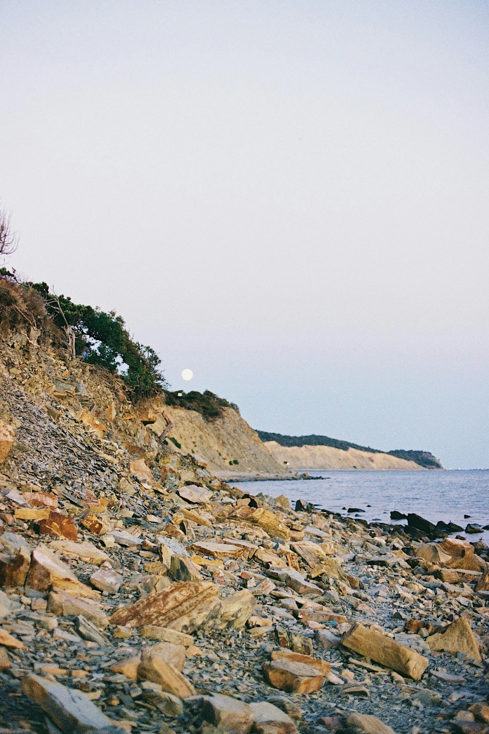 a man riding a skateboard on top of a rocky beach, a picture, inspired by Wilhelm Marstrand, unsplash, romanticism, long shot kodak portra 4 0 0, trees and cliffs, rhode island, ochre