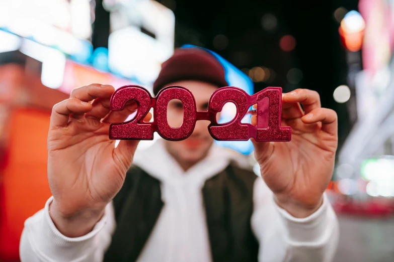 a man holding up a sign that says 2021, by Julia Pishtar, trending on pexels, new years eve, ar glasses, declan mckenna, thumbnail