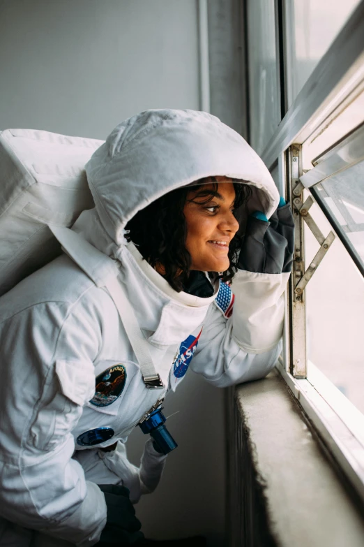 a woman in an astronaut suit looking out a window, ameera al-taweel, wearing adventure gear, apollo, belle