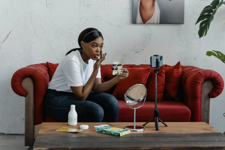 a woman sitting on a couch holding a camera, skincare, mirror and glass surfaces, avatar image, performing