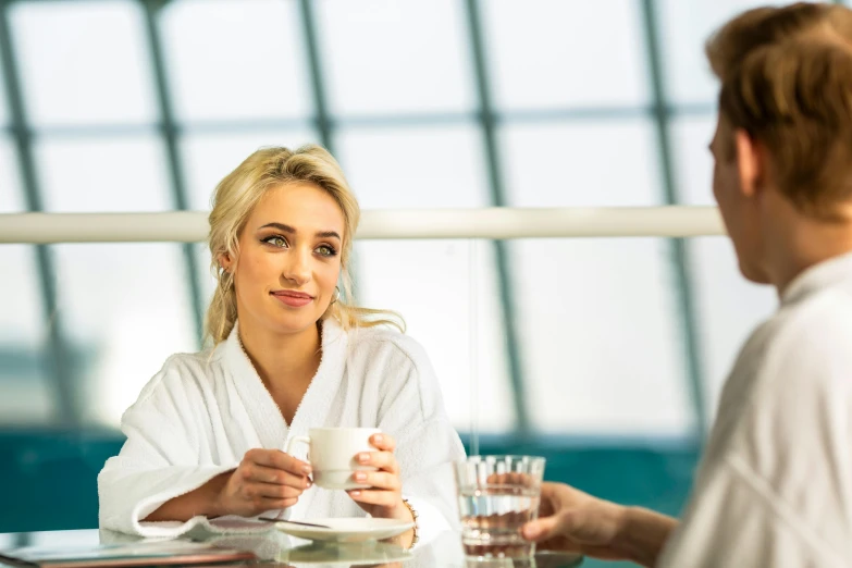 a woman sitting at a table with a cup of coffee, dirty linen robes, avalon, at the waterside, having an awkward dinner date