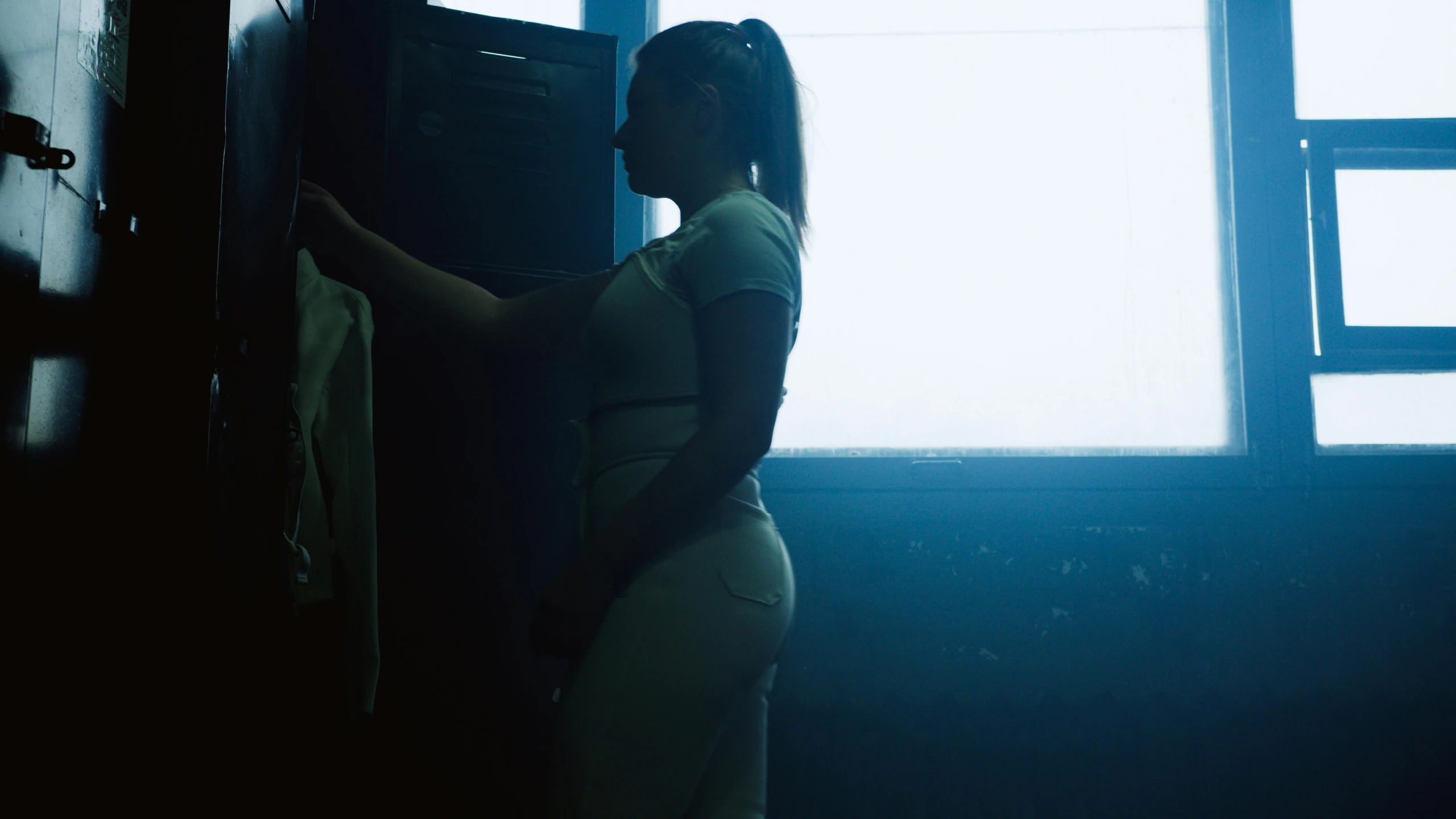 a woman standing in front of a window in a dark room, inspired by Elsa Bleda, serial art, locker room, official music video, thicc, girl wearing uniform