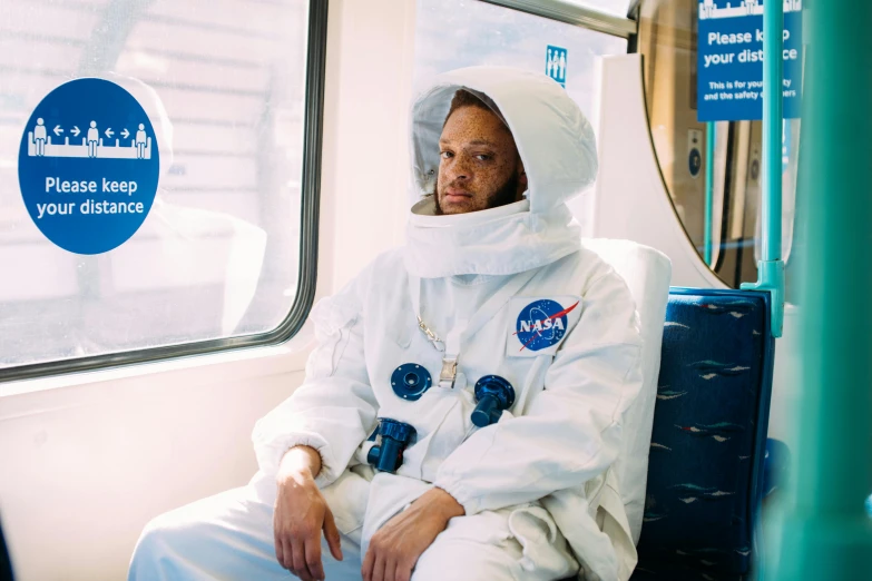 a man in a space suit sitting on a train, by Winona Nelson, trending on unsplash, afrofuturism, pete davidson, childish gambino, in style of joel meyerowitz, wearing nanotech honeycomb robe