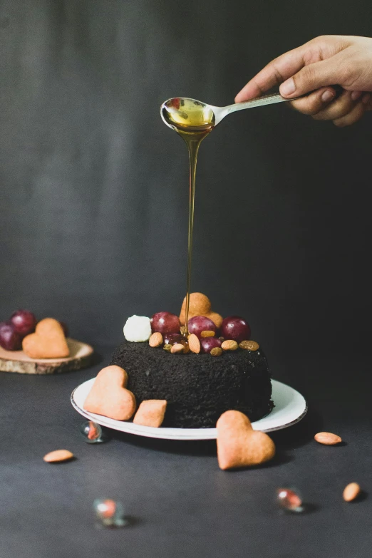 a close up of a person holding a spoon over a cake, black oil, hearts, dripping honey, serving suggestion