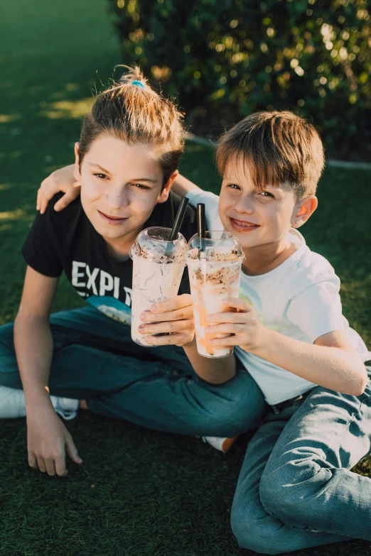 a couple of kids sitting on top of a lush green field, an album cover, pexels, drink milkshakes together, cute boys, sparkling water, avatar image