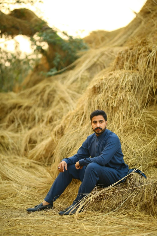 a man sitting on top of a pile of hay, an album cover, inspired by Ahmed Karahisari, pexels contest winner, qajar art, wearing a track suit, handsome, portait photo profile picture, farms