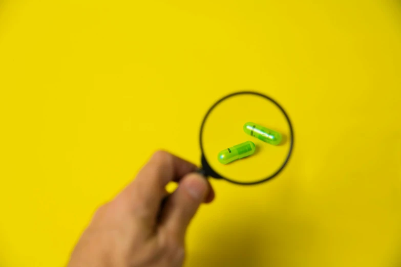 a person holding a magnifying glass over a green pill, by Adam Marczyński, pexels, synchromism, bolts of bright yellow fish, with fluo colored details, minimalist photorealist, pills