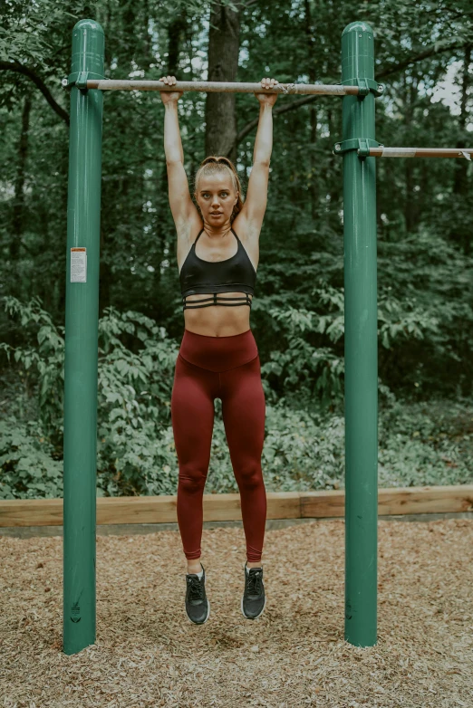 a woman doing pull ups on a pull up bar, by Jessie Algie, trending on pexels, maroon, a park, high textured, low quality photo