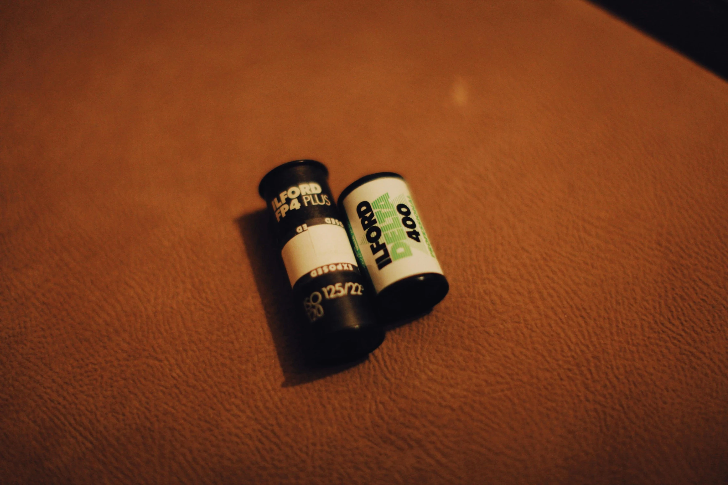 a couple of batteries sitting on top of a brown surface, a picture, inspired by Elsa Bleda, unsplash, visual art, vhs filter, greenish expired film, wide angle lens glow in the dark, black and white gainy film