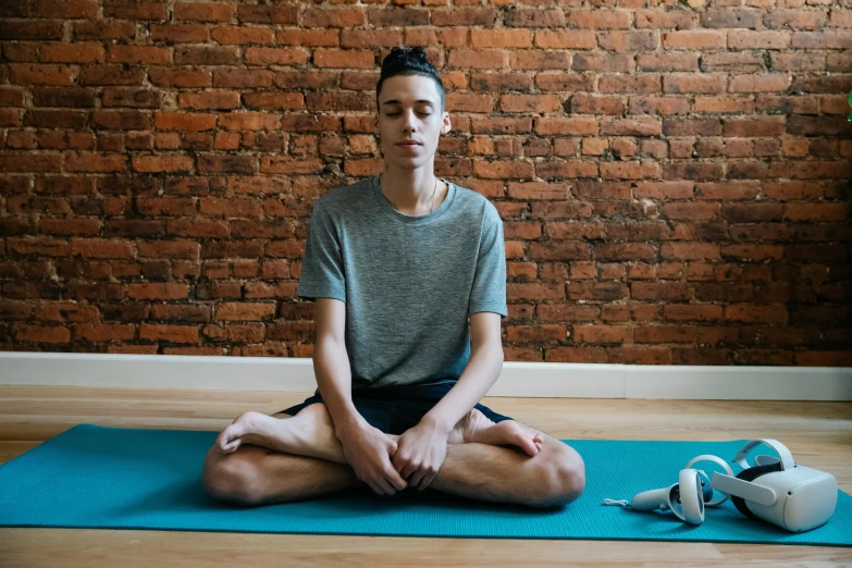 a man sitting on a yoga mat in front of a brick wall, by Nina Hamnett, pexels contest winner, hurufiyya, male teenager, calm face, ignant, nanae kawahara