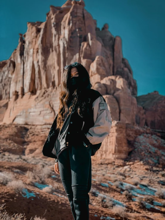 a woman standing in front of a rock formation, by Kyle Lambert, trending on unsplash, :: madison beer, wearing a dark hood, style of monument valley, she wears a jacket