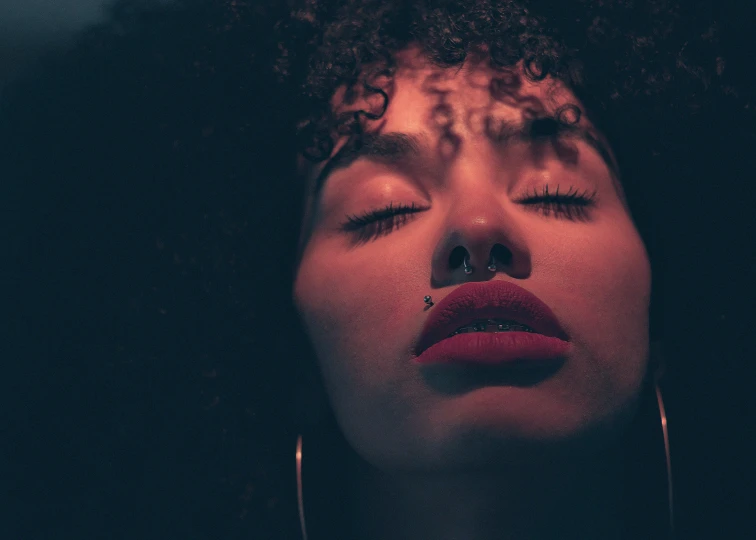 a close up of a woman with her eyes closed, inspired by Elsa Bleda, trending on pexels, afrofuturism, dark red lips, curly bangs, mid night, piercing