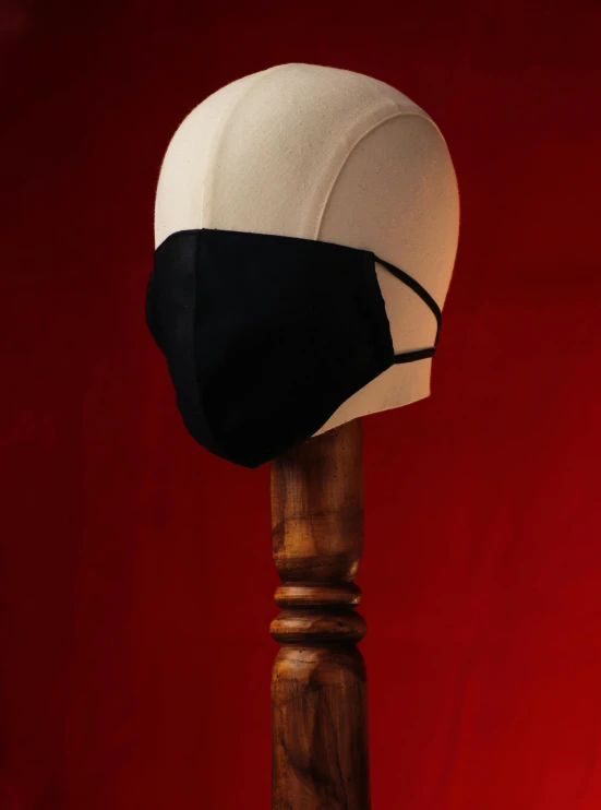 a black and white hat sitting on top of a wooden pole, face mask, in style of robert mapplethorpe, product view, against dark background