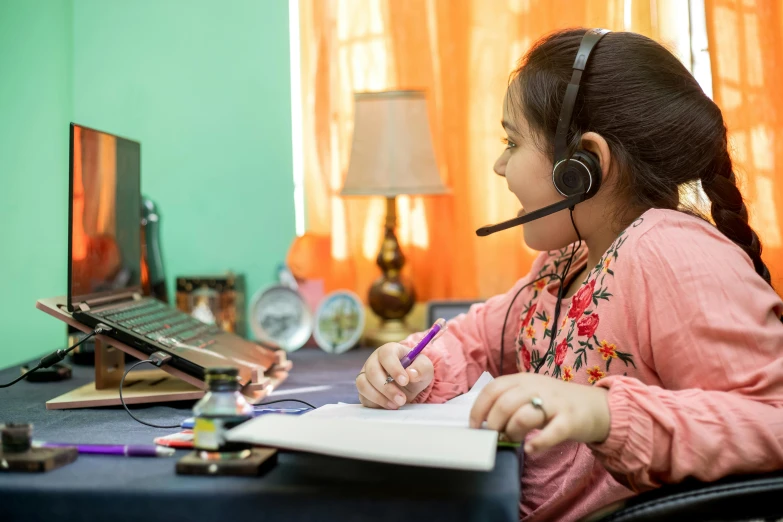 a little girl sitting at a desk in front of a laptop, by Meredith Dillman, pexels, wearing headset, india, teaching, afp