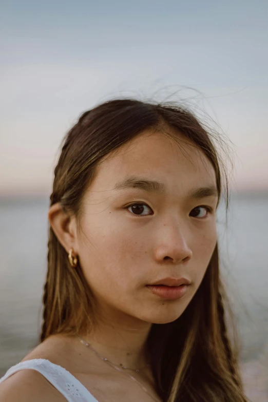 a woman standing in front of a body of water, inspired by Kim Tschang Yeul, trending on pexels, hyperrealism, pronounced cheekbones, at dusk at golden hour, portrait of a japanese teen, inuit