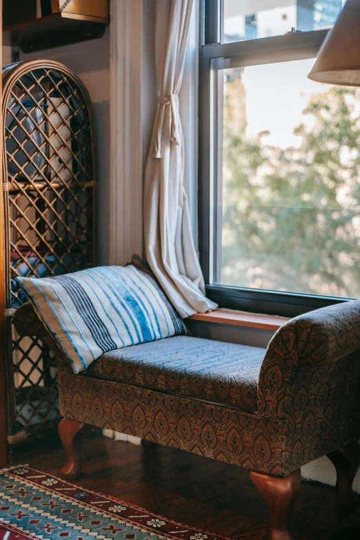 a chair sitting in front of a window next to a lamp, inspired by Riad Beyrouti, unsplash, arts and crafts movement, bay window sofa, greek fabric, brown and cyan blue color scheme, bookshelf