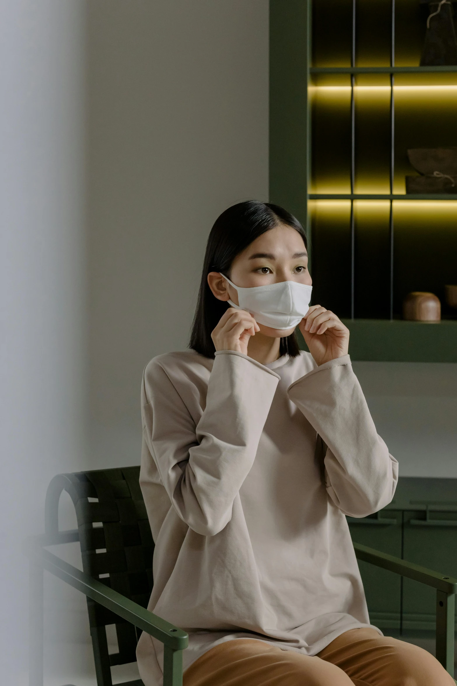 a woman sitting in a chair wearing a face mask, by Jang Seung-eop, pexels contest winner, happening, wearing a white sweater, small chin, at the counter, on a gray background