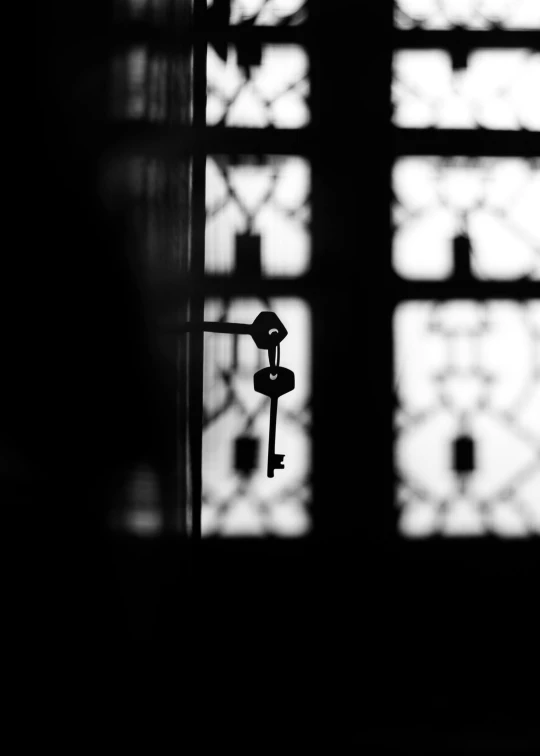 a black and white photo of a key in front of a window, by Ahmed Yacoubi, pexels contest winner, symbolism, silhouette :7, door, islamic, indoor shot