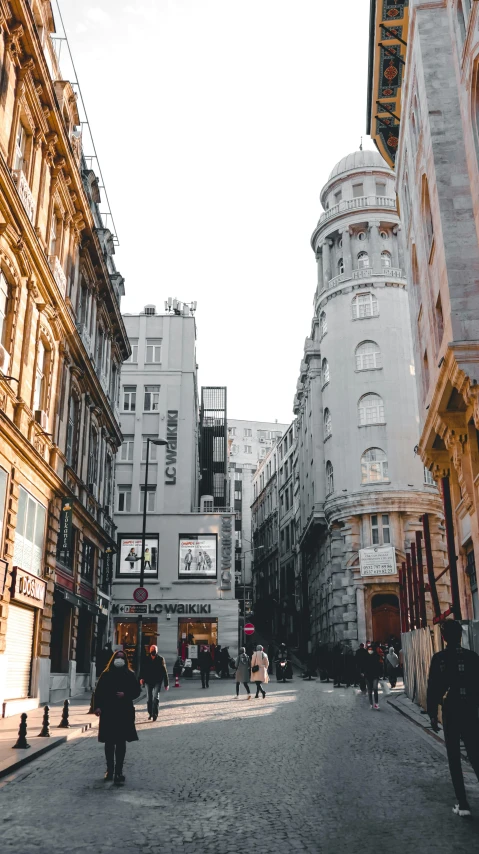 a group of people walking down a street next to tall buildings, by Adam Szentpétery, pexels contest winner, art nouveau, vienna city, stores, buildings carved out of stone, 2 0 0 0's photo