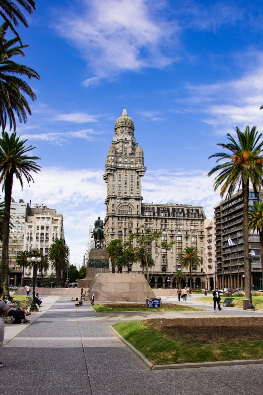 a city square with palm trees and a clock tower, inspired by Maties Palau Ferré, art nouveau, buenos aires, grass field surrounding the city, taller than a skyscraper, baroque winding cobbled streets