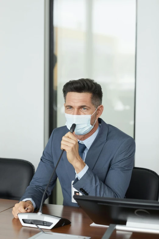 a man in a suit sitting at a table with a microphone, face mask, clean medical environment, thumbnail, luka mivsek