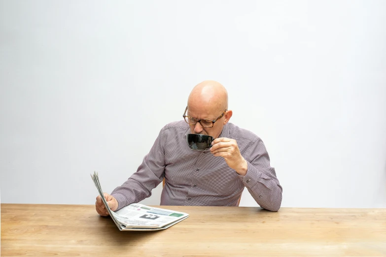 a man sitting at a table in front of a laptop computer, unsplash, private press, bald man, reading the newspaper, on a pale background, drinking