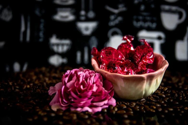 a bowl of candy sitting on top of a pile of coffee beans, a still life, by Julia Pishtar, art photography, red and magenta flowers, thumbnail, foil, culinary art photography